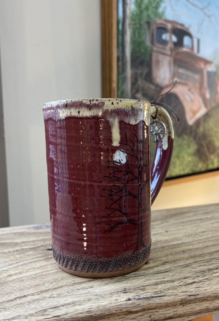 A red mug sits on a table next to a painting.