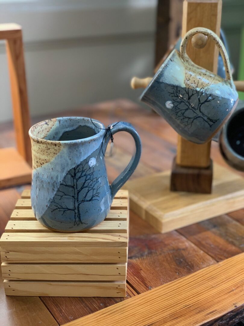 A mug with a tree on it sits on a wooden table.