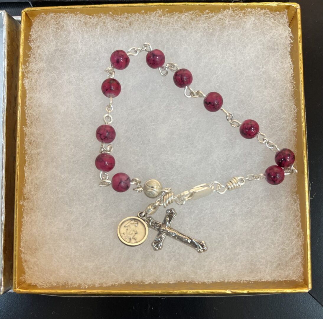 A rosary bracelet in a box with a cross and rosary beads.