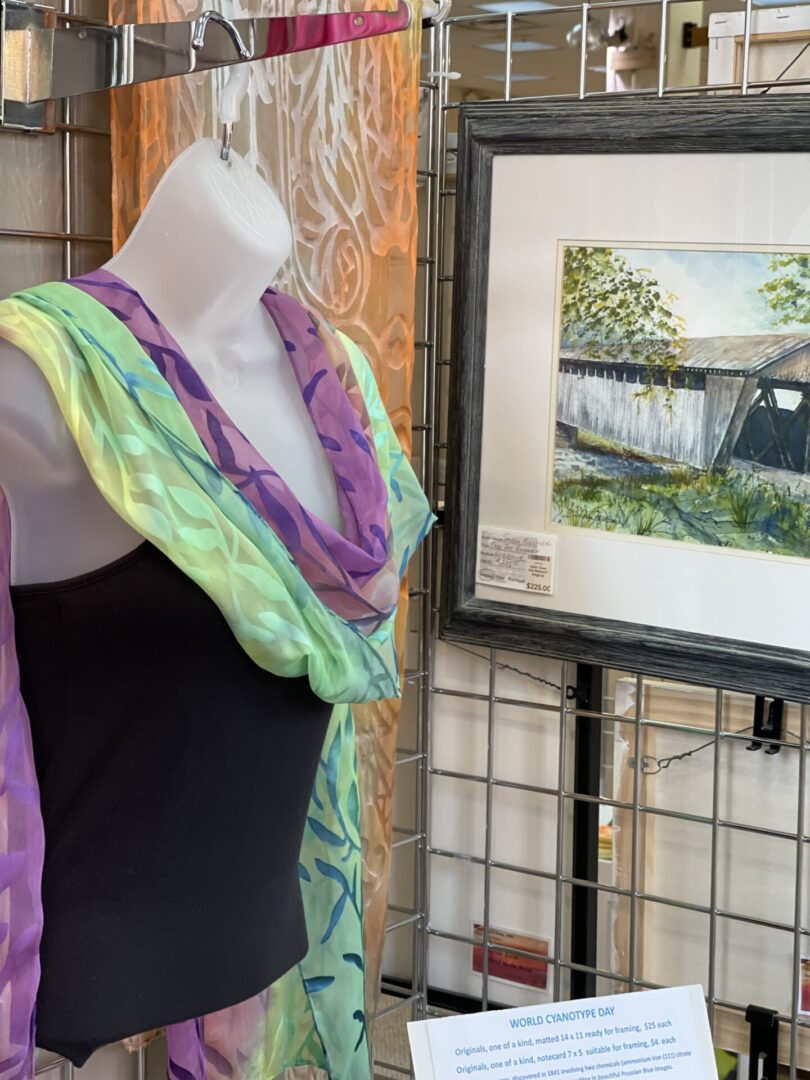 A scarf is displayed on a mannequin with a painting.