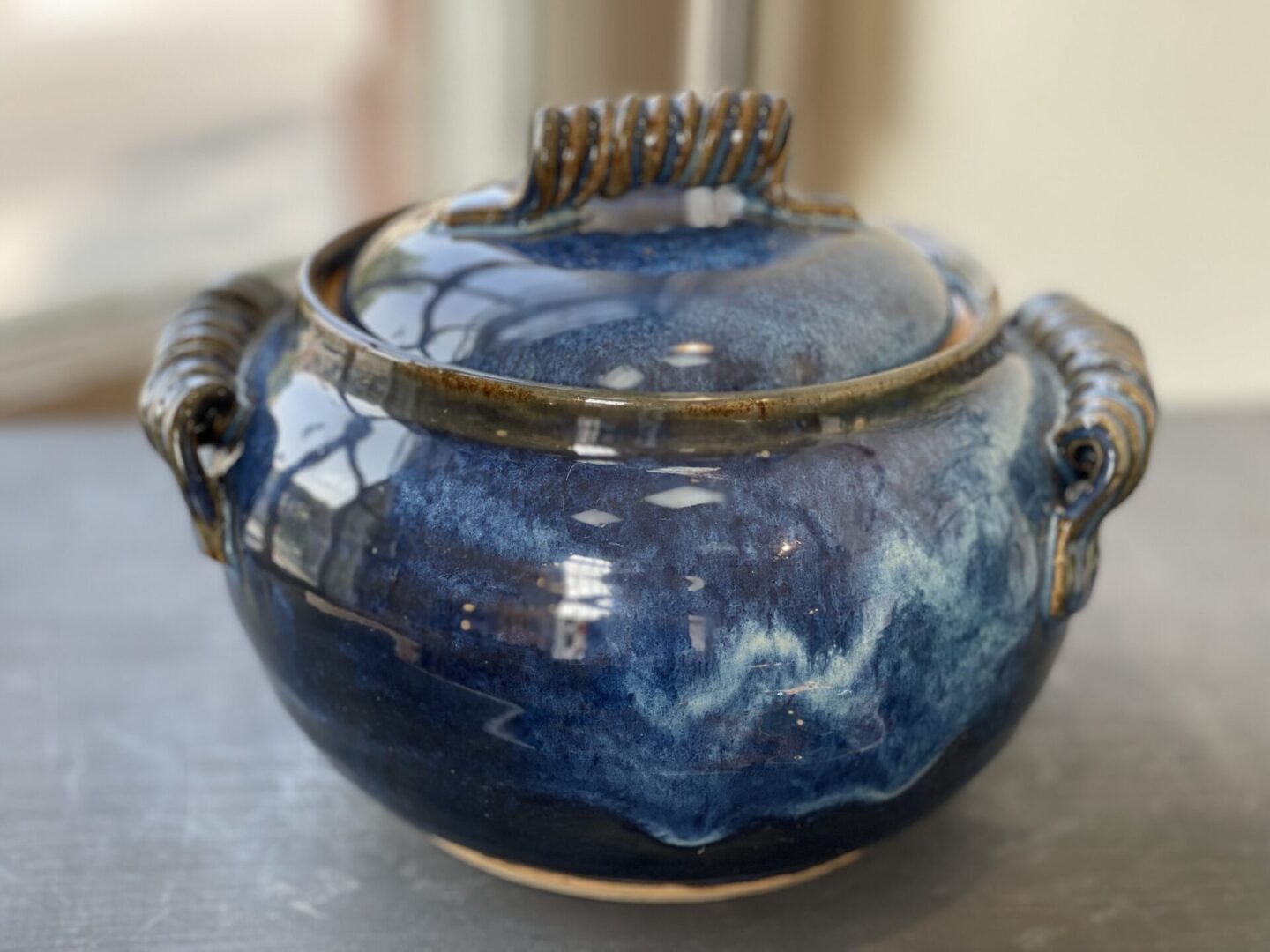 A blue ceramic jar with a handle on a table.